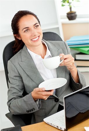 simsearch:400-04386602,k - Businesswoman holding a cup of coffee in front of her laptop sitting at her desk in her office Stockbilder - Microstock & Abonnement, Bildnummer: 400-04217182