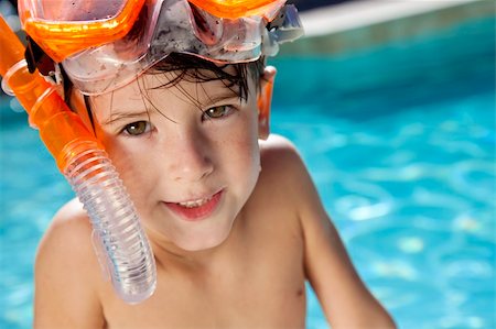 smile as mask for boy - A happy young boy relaxing on the side of a swimming pool wearing orange goggles and snorkel Stock Photo - Budget Royalty-Free & Subscription, Code: 400-04219473