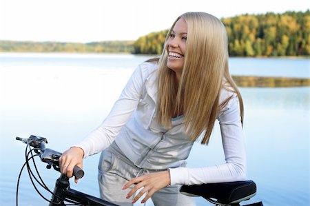 simsearch:400-04336561,k - Young smiling woman holds the bicycle at still blue lake Fotografie stock - Microstock e Abbonamento, Codice: 400-04210474