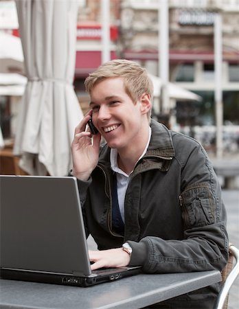 Happy young man speaking on cellphone in a street cafe while working with his laptop Stock Photo - Budget Royalty-Free & Subscription, Code: 400-04213671
