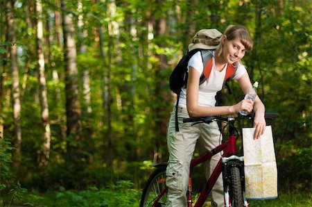 beautiful young woman sitting on her bicycle with bottle of water in hand and map in the middle of summer forest Fotografie stock - Microstock e Abbonamento, Codice: 400-04227630