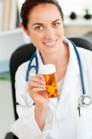simsearch:400-05892402,k - Delighted female doctor holding pills into the camera in her office sitting at her desk Stock Photo - Budget Royalty-Free & Subscription, Code: 400-04220813