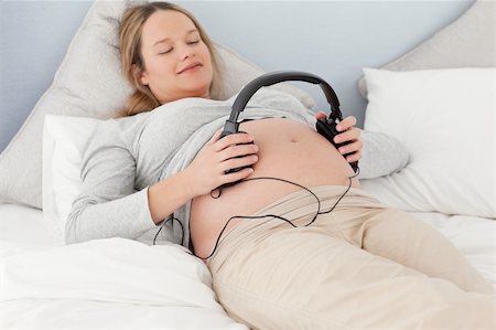 simsearch:400-04767824,k - Happy future mom putting headphones on her belly lying on a bed Foto de stock - Royalty-Free Super Valor e Assinatura, Número: 400-04235207