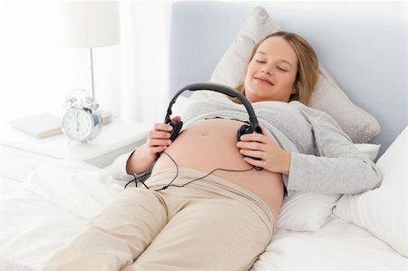 simsearch:400-04767824,k - Smiling future mom putting headphones on her belly lying on a bed Foto de stock - Royalty-Free Super Valor e Assinatura, Número: 400-04235222
