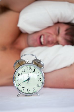 simsearch:400-04287303,k - Angry young man lying in bed and annoyed by his alarm clock in the bedroom at home Stock Photo - Budget Royalty-Free & Subscription, Code: 400-04235874