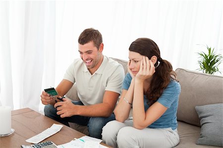 simsearch:400-05746763,k - Happy man cutting his credit card with scissors with his girlfriend on the sofa at home Stock Photo - Budget Royalty-Free & Subscription, Code: 400-04237360