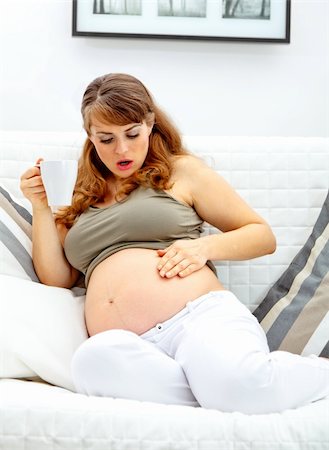 pregnant surprise - Surprised beautiful pregnant woman sitting on sofa at home and  holding cup of tea in hand Stock Photo - Budget Royalty-Free & Subscription, Code: 400-04233446
