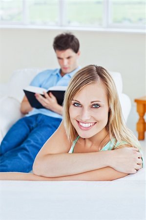 simsearch:400-04202081,k - Girlfriend smiling at the camera while her boyfriend is focused on a  book sitting in the background Foto de stock - Royalty-Free Super Valor e Assinatura, Número: 400-04256051