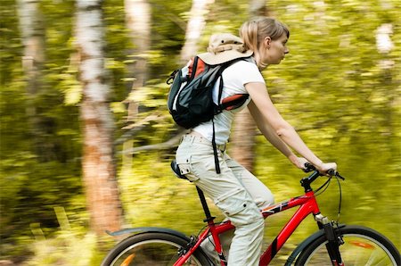 beautiful young woman riding her bicycle in forest, motion blured background, some blur on girl Fotografie stock - Microstock e Abbonamento, Codice: 400-04259277