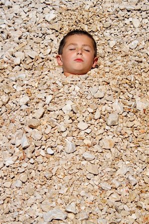 boy buried in the pebbles on the beach Stock Photo - Budget Royalty-Free & Subscription, Code: 400-04265640