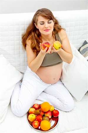 simsearch:400-05911635,k - Beautiful pregnant woman sitting on sofa at home and enjoying fruits Foto de stock - Super Valor sin royalties y Suscripción, Código: 400-04266473