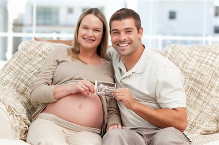 simsearch:400-07322828,k - Cheerful couple of future parents holding an echography sitting on the sofa Fotografie stock - Microstock e Abbonamento, Codice: 400-04266845