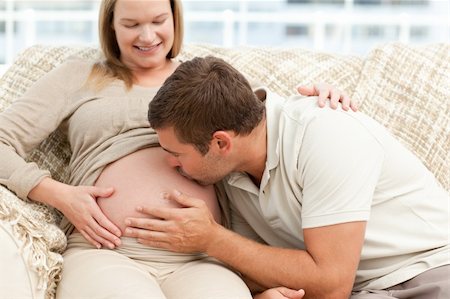 simsearch:400-04266840,k - Future dad kissing the belly of his wife sitting on the sofa in the living room Photographie de stock - Aubaine LD & Abonnement, Code: 400-04266840