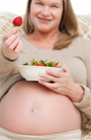 simsearch:400-04266869,k - Future mom showing a strawberry to the camera sitting on the sofa Stock Photo - Budget Royalty-Free & Subscription, Code: 400-04266872