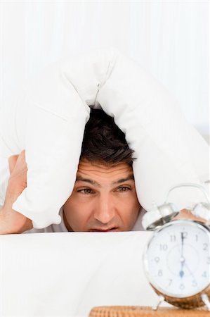 simsearch:400-04287303,k - Handsome man looking at his alarm clock with head under the pillow Stockbilder - Microstock & Abonnement, Bildnummer: 400-04266908