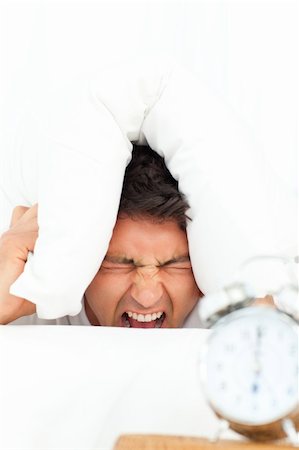 simsearch:400-04287303,k - Man stressed by his alarm clock putting his head under the pillow in the bedroom Stockbilder - Microstock & Abonnement, Bildnummer: 400-04266912