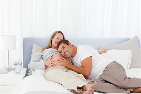 Funny man putting his head on the belly of his pregnant wife while relaxing on the bed Stock Photo - Budget Royalty-Free & Subscription, Code: 400-04267440