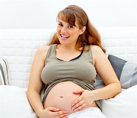 simsearch:400-05911635,k - Smiling beautiful pregnant female sitting on sofa at home and touching her belly Foto de stock - Super Valor sin royalties y Suscripción, Código: 400-04268419