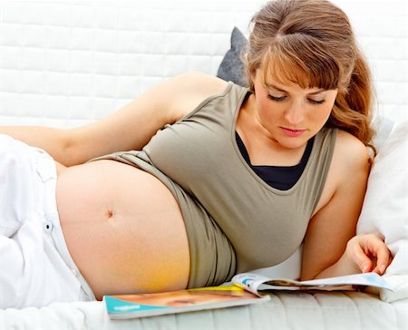 simsearch:400-04688796,k - Beautiful pregnant woman lying on sofa at home with magazine Fotografie stock - Microstock e Abbonamento, Codice: 400-04268432
