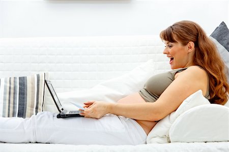 pregnant mom on computer - Pleased beautiful pregnant woman sitting on sofa at home with laptop and credit card Stock Photo - Budget Royalty-Free & Subscription, Code: 400-04268442