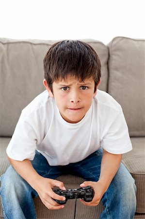 Cute boy playing video games sitting on the sofa at home Stock Photo - Budget Royalty-Free & Subscription, Code: 400-04268932