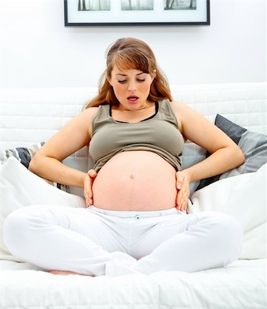 pregnant surprise - Surprised  beautiful pregnant woman sitting on sofa at home and holding her belly. Stock Photo - Budget Royalty-Free & Subscription, Code: 400-04262657