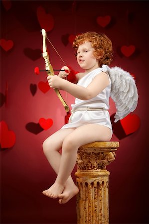Small aiming boy in an image of the cupid on a red background Fotografie stock - Microstock e Abbonamento, Codice: 400-04262978