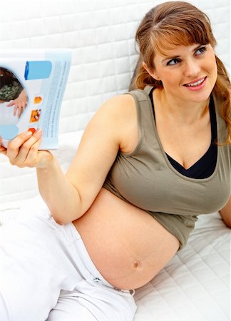 simsearch:400-05911635,k - Smiling beautiful pregnant woman relaxing on couch at home with magazine. Foto de stock - Super Valor sin royalties y Suscripción, Código: 400-04277515