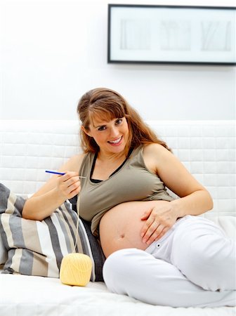 simsearch:400-04859723,k - Smiling beautiful pregnant woman sitting on sofa and knitting for her baby. Fotografie stock - Microstock e Abbonamento, Codice: 400-04285093