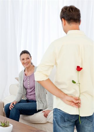 simsearch:400-04151970,k - Passionate man hidden a rose behind his back for his grilfriend sitting in the living room Fotografie stock - Microstock e Abbonamento, Codice: 400-04287284