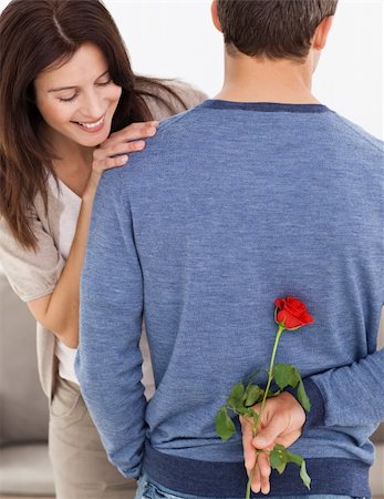 simsearch:400-04151970,k - Attentive man hiding a flower behind his back for his impatiente girlfriend in the living room Fotografie stock - Microstock e Abbonamento, Codice: 400-04287299