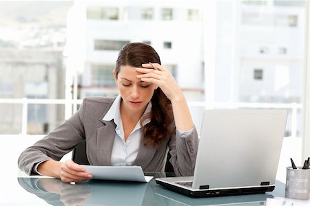 simsearch:400-04562604,k - Pensive businesswoman looking at a paper while working on her laptop at her desk Photographie de stock - Aubaine LD & Abonnement, Code: 400-04281574