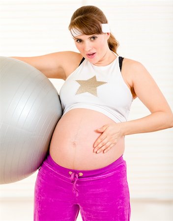 Surprised beautiful pregnant female holding fitness ball and touching her belly at living room Stock Photo - Budget Royalty-Free & Subscription, Code: 400-04282574