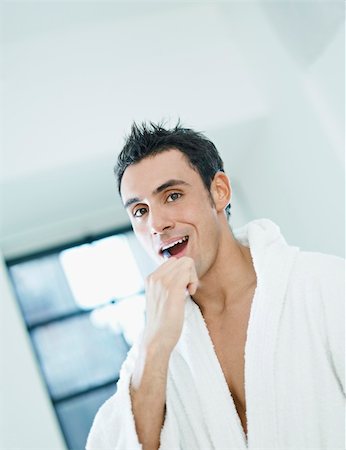 caucasian adult man with bathrobe brushing teeth in bathrooom and looking at camera. Vertical shape, waist up, copy space Stock Photo - Budget Royalty-Free & Subscription, Code: 400-04282844