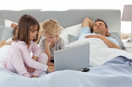 Attentive boy using a laptop with his sister while their parents are sleeping in the bed Stock Photo - Budget Royalty-Free & Subscription, Code: 400-04296638