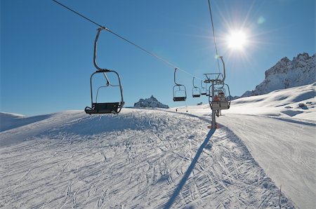 Chair ski lift driving over ski slope in the Dolomiti. Sun in the front. Skiers. Blue sky. Photographie de stock - Aubaine LD & Abonnement, Code: 400-04304055