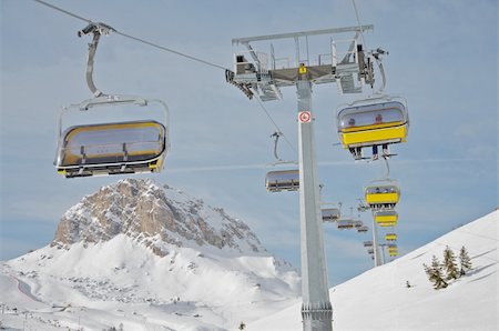 ski hill with chair lift - Ski chair lift in the Dolomites. Yellow chairs. Skiers traveling. Blue sky with mountain in the background. Stock Photo - Budget Royalty-Free & Subscription, Code: 400-04304062