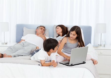 Childrens looking at their laptop while parents are talking on the bed Stock Photo - Budget Royalty-Free & Subscription, Code: 400-04300901