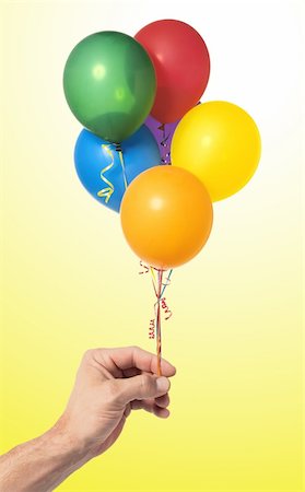 simsearch:400-04713054,k - Hand holding colorful air balloons over yellow background Photographie de stock - Aubaine LD & Abonnement, Code: 400-04317199