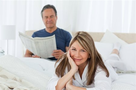 simsearch:400-05314664,k - Smiling woman looking at the camera while her husband is reading at home Stock Photo - Budget Royalty-Free & Subscription, Code: 400-04310934