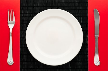 scenic dinner - empty white plate on black table with knife and fork on red napkin by the sides of the plate Stock Photo - Budget Royalty-Free & Subscription, Code: 400-04323509