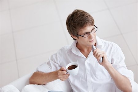 A young man with a cup of coffee and a remote control in hand Stock Photo - Budget Royalty-Free & Subscription, Code: 400-04336289