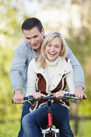 simsearch:400-04336549,k - Young attractive couple rides a bicycle in the park Fotografie stock - Microstock e Abbonamento, Codice: 400-04336554