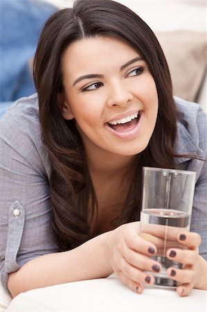 simsearch:400-04340722,k - Portrait of a beautiful young Latina Hispanic woman laying down on a sofa, laughing and drinking a glass of water Stock Photo - Budget Royalty-Free & Subscription, Code: 400-04336706