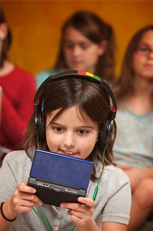 preteen girls tongue - Little Caucasian girl with earphones plays a handheld video game Stock Photo - Budget Royalty-Free & Subscription, Code: 400-04339485