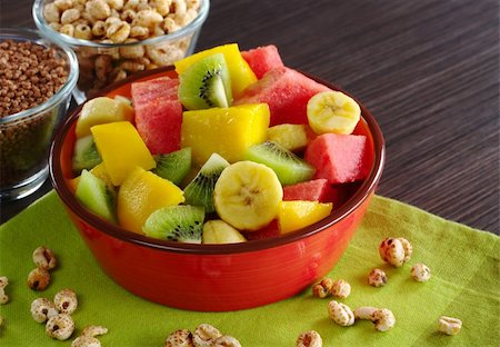 Fresh fruit salad made of banana, kiwi, watermelon and mango pieces in orange bowl with cereals (puffed wheat and puffed chocolate quinoa) (Selective Focus, Focus on the front of the bowl and the fruits in the front) Photographie de stock - Aubaine LD & Abonnement, Code: 400-04345439