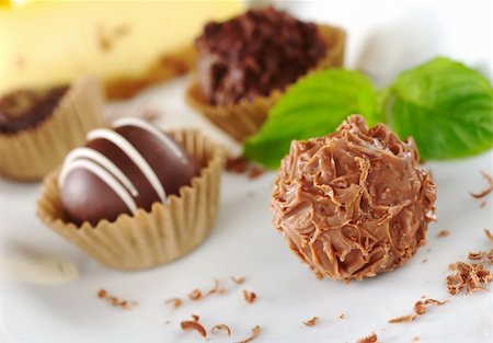Chocolate truffles with mint leaf, fine chocolate shavings and a yellow cake in the background (Very Shallow Depth of Field, Focus on the front of the first praline) Stock Photo - Budget Royalty-Free & Subscription, Code: 400-04345442