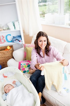Joyful woman sitting on the sofa with bags reading a card while her baby is sleeping in his cradle Stock Photo - Budget Royalty-Free & Subscription, Code: 400-04341609