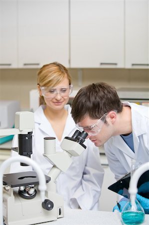 simsearch:400-05670345,k - Caucasian scientists holding clipboard and looking through a microscope in their laboratory Photographie de stock - Aubaine LD & Abonnement, Code: 400-04341800