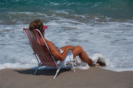 A tanned, fit, older woman relaxes in a beach chair as waves lap around her feet. Photographie de stock - Aubaine LD & Abonnement, Code: 400-04355448